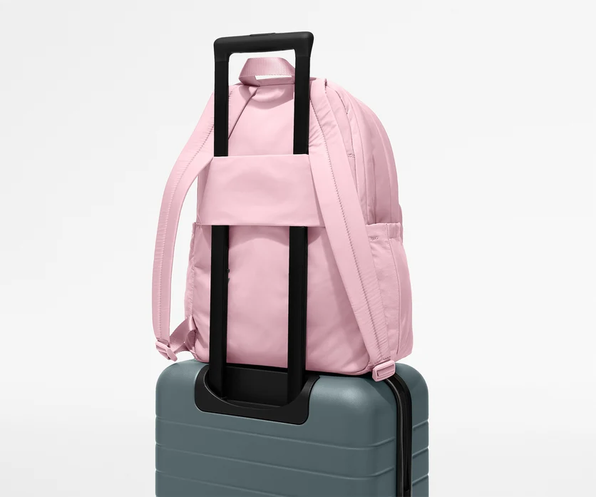 Pink backpack with black handle on a gray suitcase against a white background