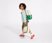 A child model wearing the Kids Backpack in Marshmallow White with the chest strap in use and holds the Kids Lunch Box in Marshmallow White